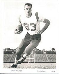 Black-and-white photograph of Infante wearing a football uniform with pads (but no helmet), with a number 33 jersey, and cradling a football in his right arm