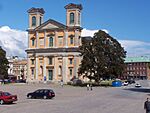 A church in the middle of the square, some cars parked in front