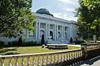 A white stone library with a green dome on top and two lions in front surrounded by grass and bushes