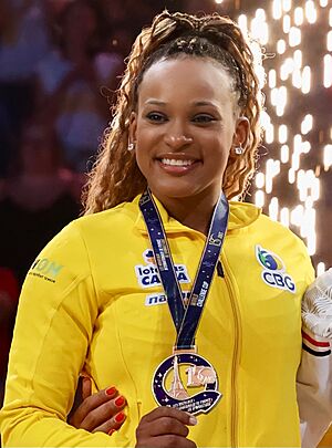 Andrade with a gold medal. She is a dark-skinned woman in her mid twenties with curly, brown hair wearing a yellow sports jersey.