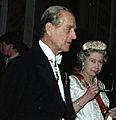 Elizabeth, in formal dress, holds a pair of spectacles to her mouth in a thoughtful pose