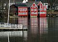 Three bright red buildings stand across the river from the photographer; one of them has a sign saying "Lowell's Boat Shop".