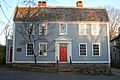 The front of a two story gray house with white trim. The front and side doors are red.