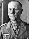 The head and shoulders of an elderly man, shown in semi-profile. He wears a peaked cap and a military uniform with an Eagle above his right and various military decorations above left breast pocket, and an Iron Cross displayed at the front of his shirt collar. His facial expression is a determined; his eyes are looking into the distance to the left of the camera.