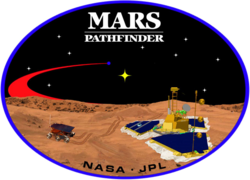 An image inside an oval, depicting two spacecraft, one a lander, and one a rover, on the surface of Mars. The words "Mars Pathfinder" are written on the top and the words "NASA · JPL" are written on the bottom.