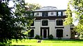 A white house with dark trim, including decorative elements. The house has three stories, and there is an octagonal element protruding above the top floor.