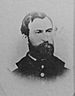 Head of a white man with a full beard and receding hairline, wearing a military jacket with large bright buttons.