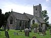 Stone building with square tower. In the foreground are gravestones.