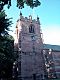 A sandstone church tower seen from a low angle with part of a tree to its left