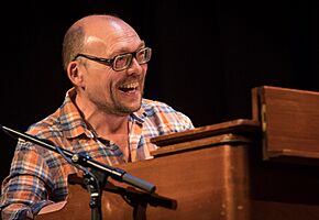 Bugge Wesseltoft wearing a light checkered shirt, sitting behind a piano, grinning broadly and looking left of camera