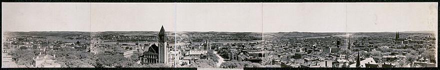 A panorama from 1909, in sepia, shows a view of the city perpendicular to the river; there are numerous church steeples and the city hall tower can be seen left of center.